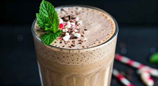 A creamy chocolate mint smoothie served in a tall glass, topped with chopped peppermint candy, chocolate shavings, and a fresh sprig of mint. Two festive red and white candy canes lie blurred in the background.