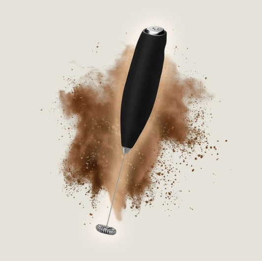 Black handheld frother with whisk, surrounded by coffee powder for perfect frothing and mixing.